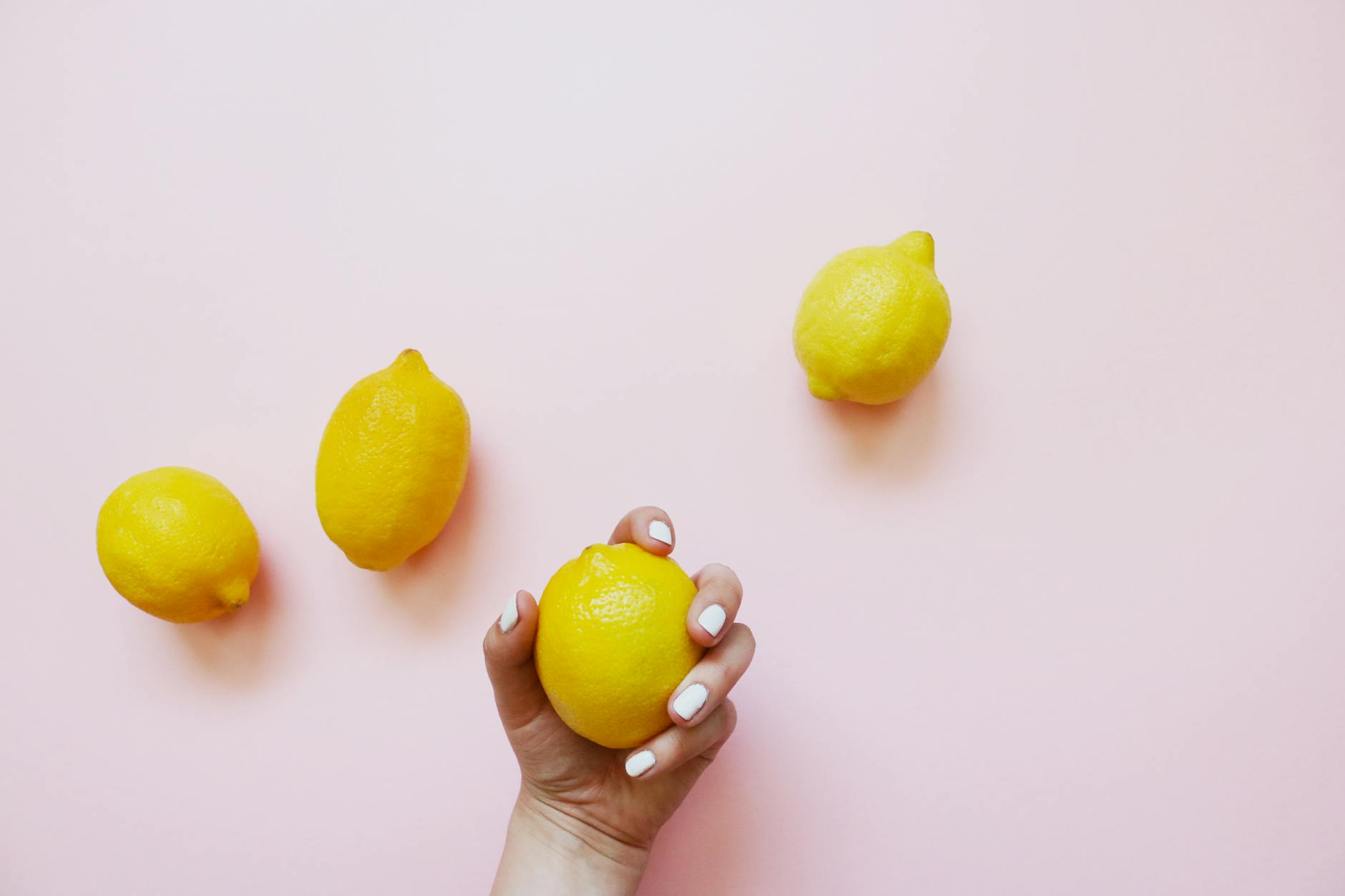 A hand holding fresh lemons on a soft pink background, symbolizing natural rhythm and cycle awareness.
