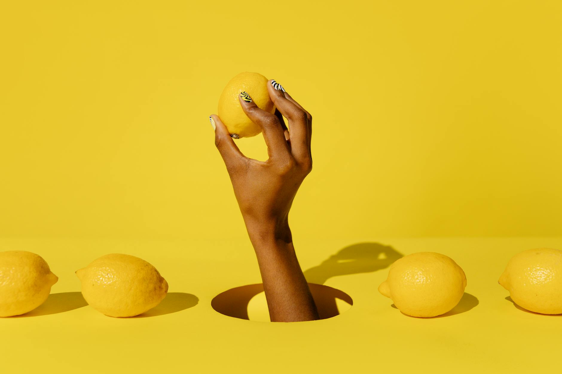 A hand holding a fresh lemon against a vivid yellow background, representing the precise nature of lemon vibrators