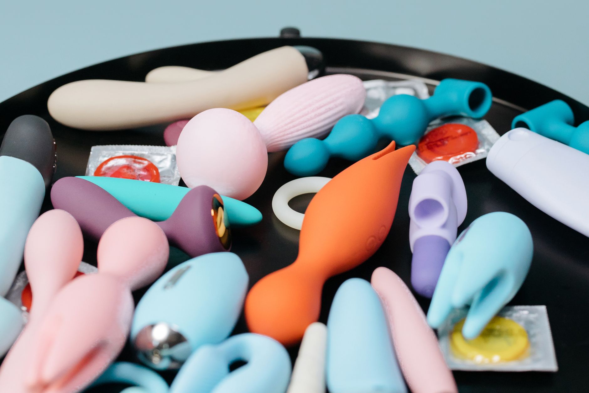 An arrangement of colorful silicone sex toys on a black surface, including various clitoral vibrators
