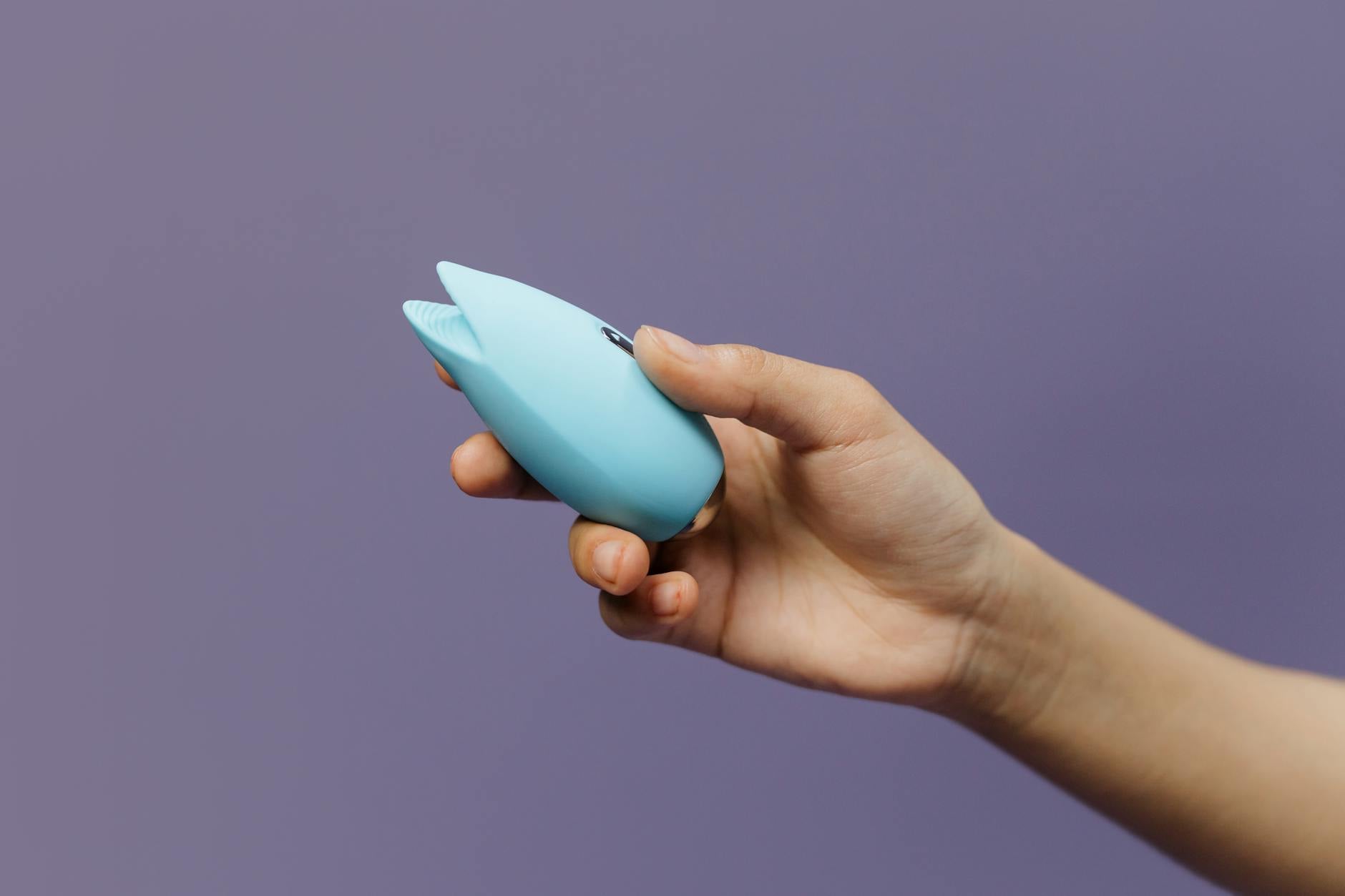 A blue lemon vibrator held in hand against a solid purple background, representing self-love and pleasure recovery