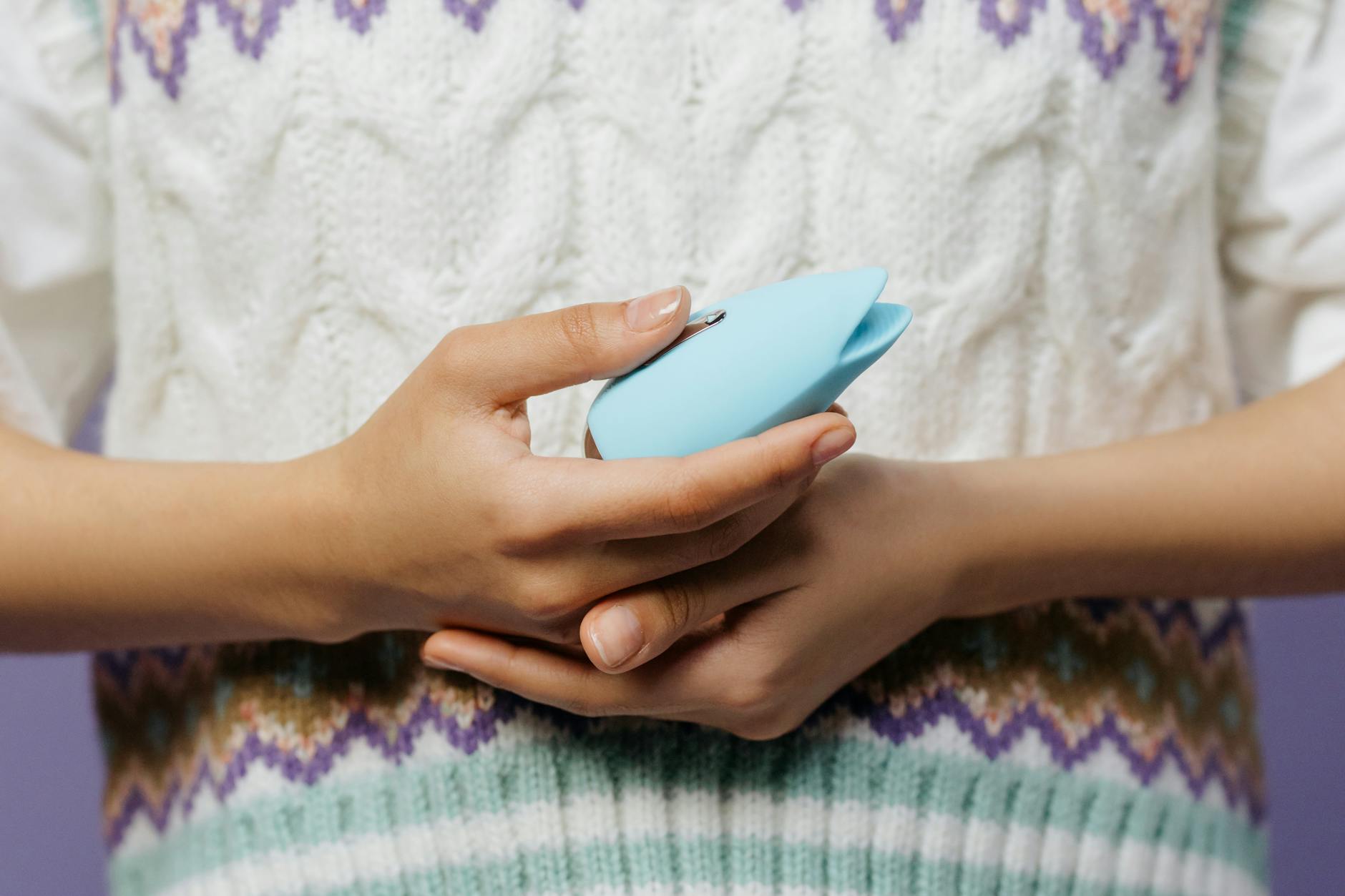 Two hands holding pink and blue silicone vibrators against a pastel background