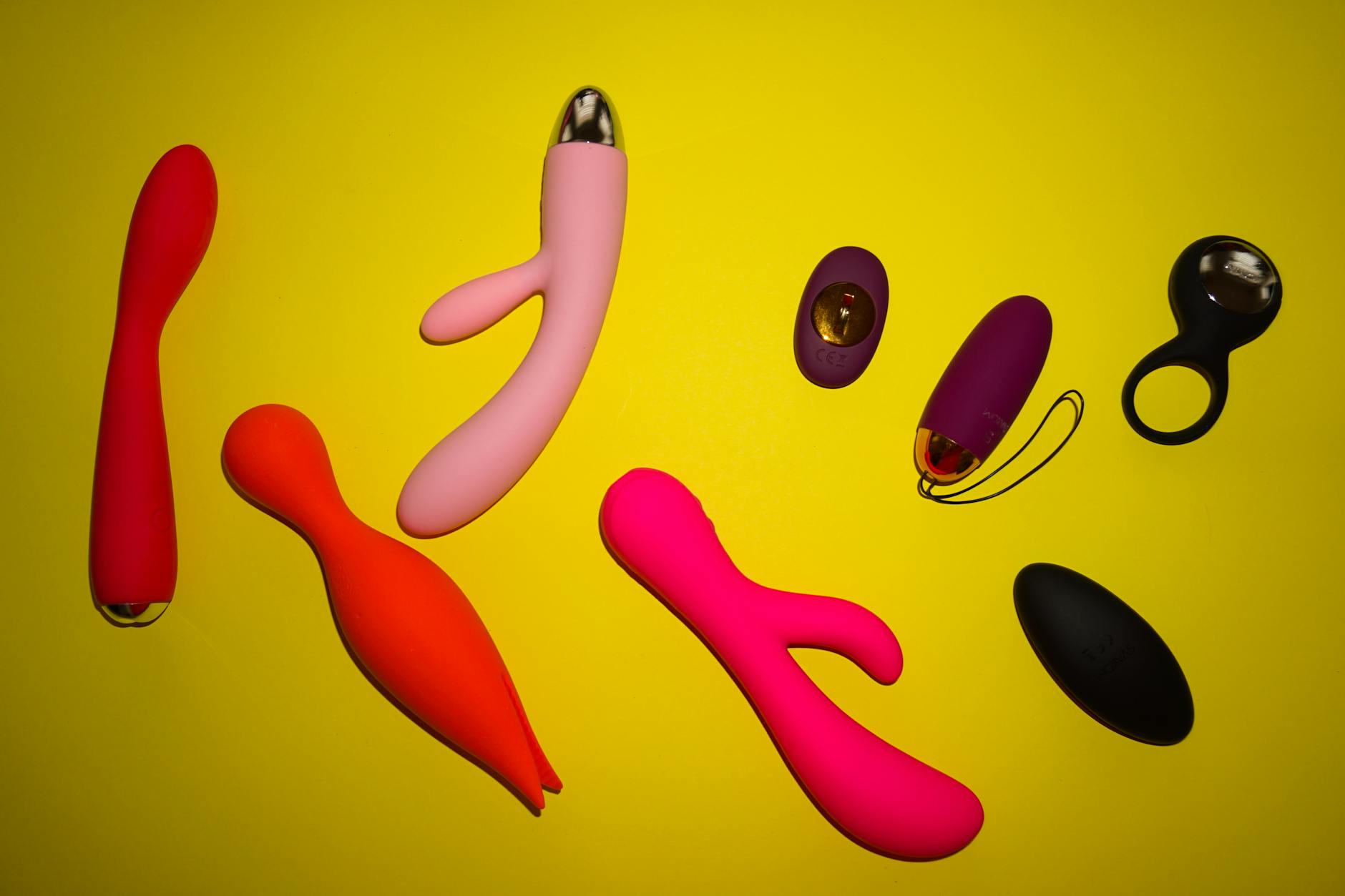 Colorful vibrators and sex toys arranged on a bright yellow surface, representing couples exploring pleasure together
